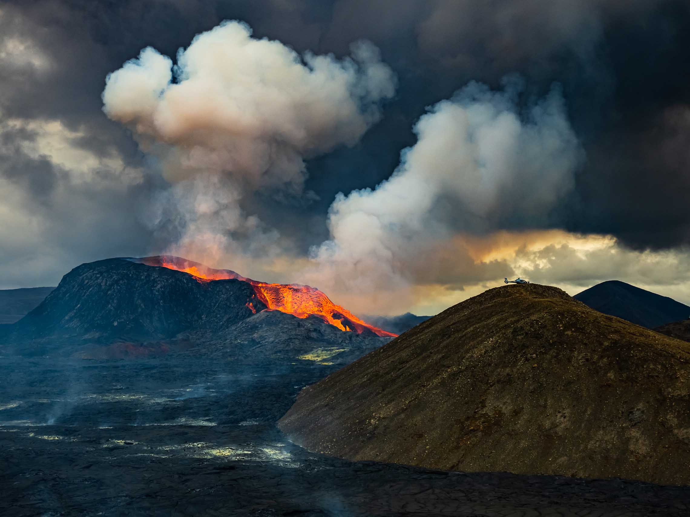 Erupting volcano in Iceland with helicopter on nearby peak